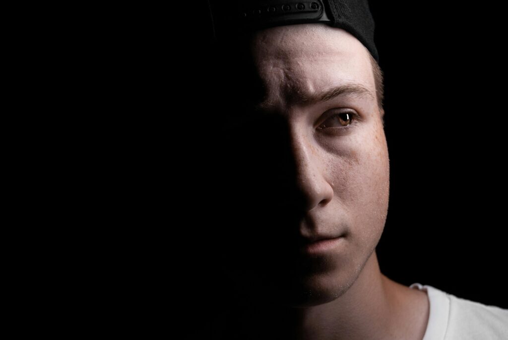 Close-up portrait of a young man in shadow with intense expression, black background.